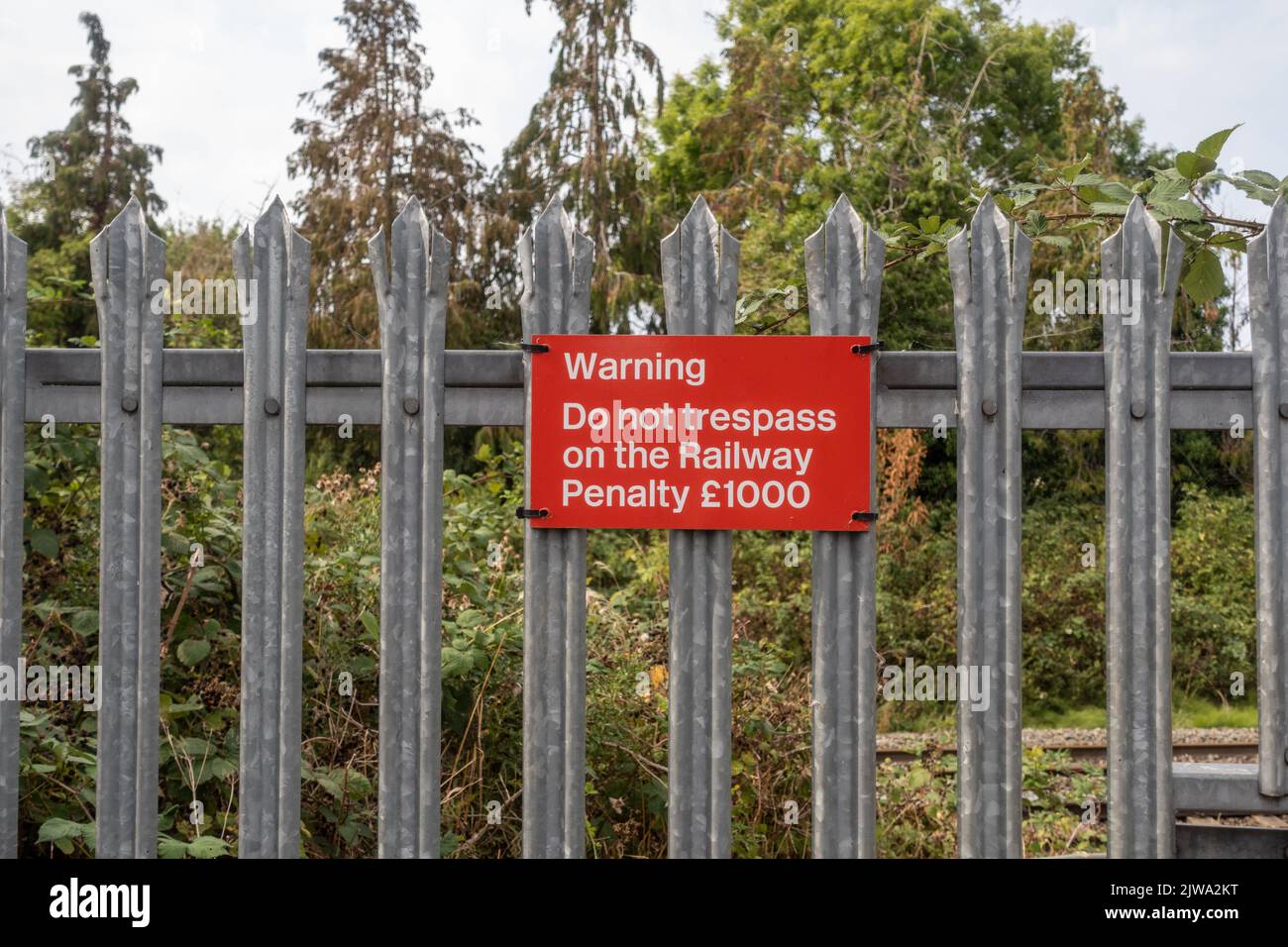 Red warning sign reading - Warning Do not trespass on the railway Penalty £1000 on metal fencing beside the railway line in Trowbridge, Wiltshire, UK Stock Photo