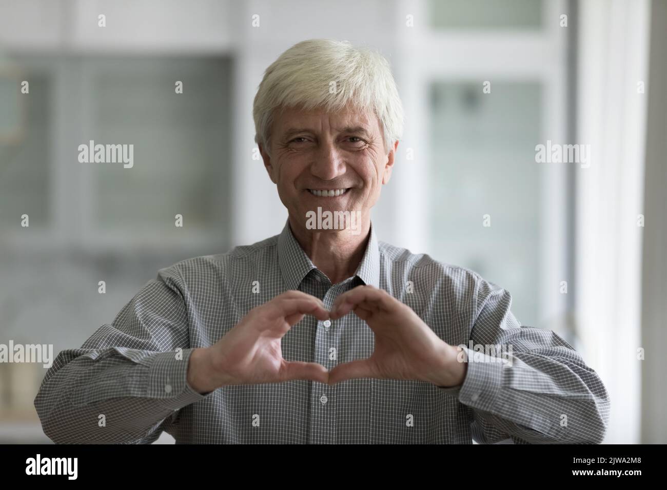 Cheerful grey haired old man showing hand heart at chest Stock Photo