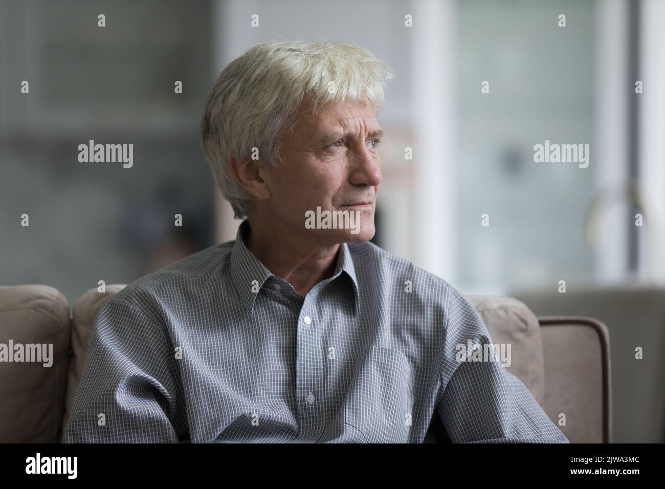 Thoughtful sad senior elder man sitting on home couch Stock Photo