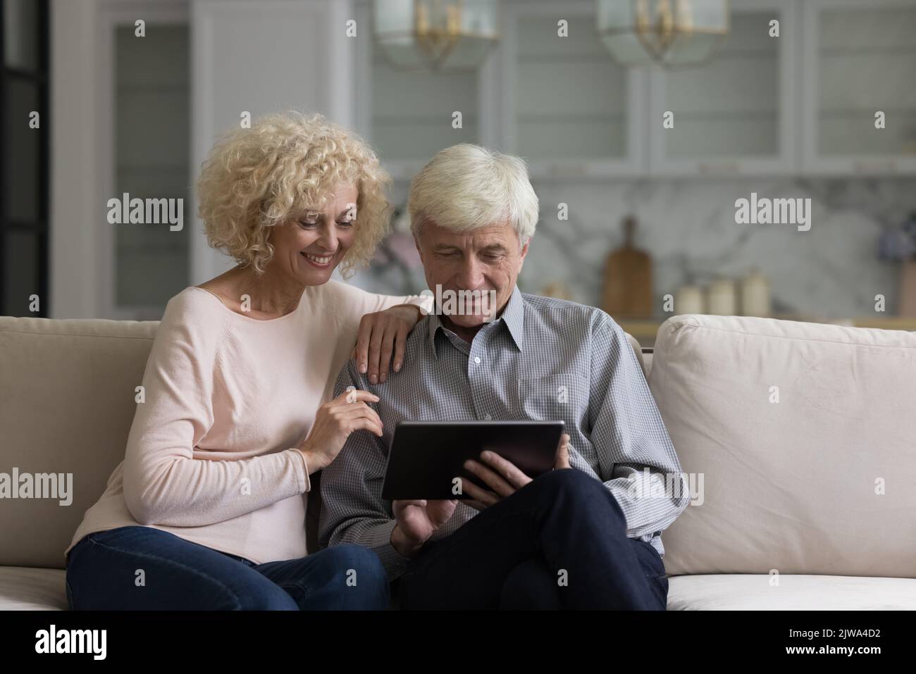 Happy senior couple using online app on tablet computer, laughing Stock Photo