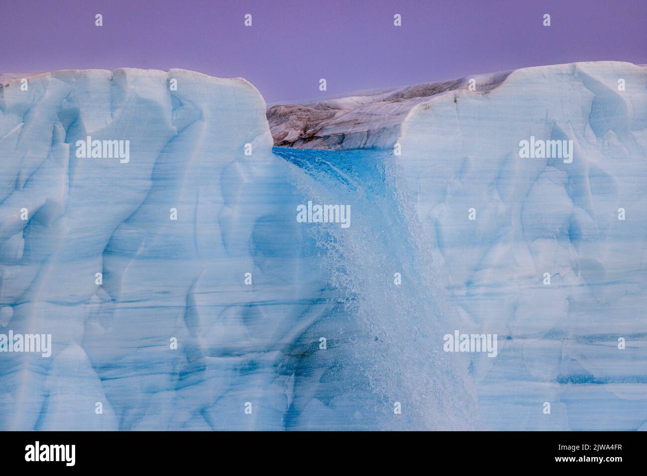 an icy blue river crosses the austfonna ice cap on nordaustlandet and crashes down to the sea at the sheer ice cliff as an enormous waterfall Stock Photo
