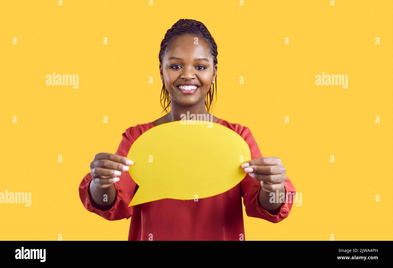 Paper blank mockup of speech bubble in hands of smiling african american woman on yellow background. Stock Photo