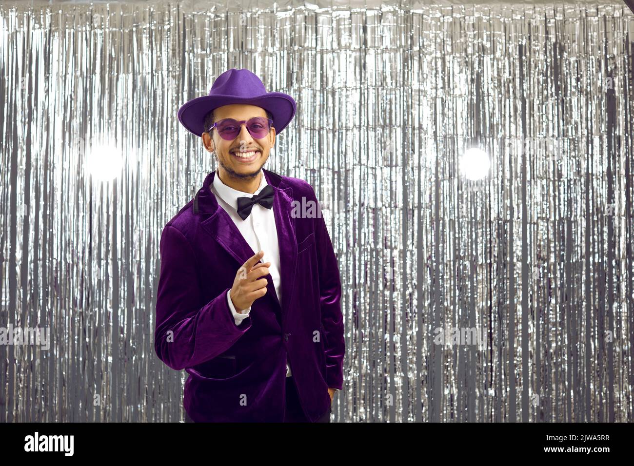 Happy man in purple suit, hat and glasses presents something on blank background Stock Photo