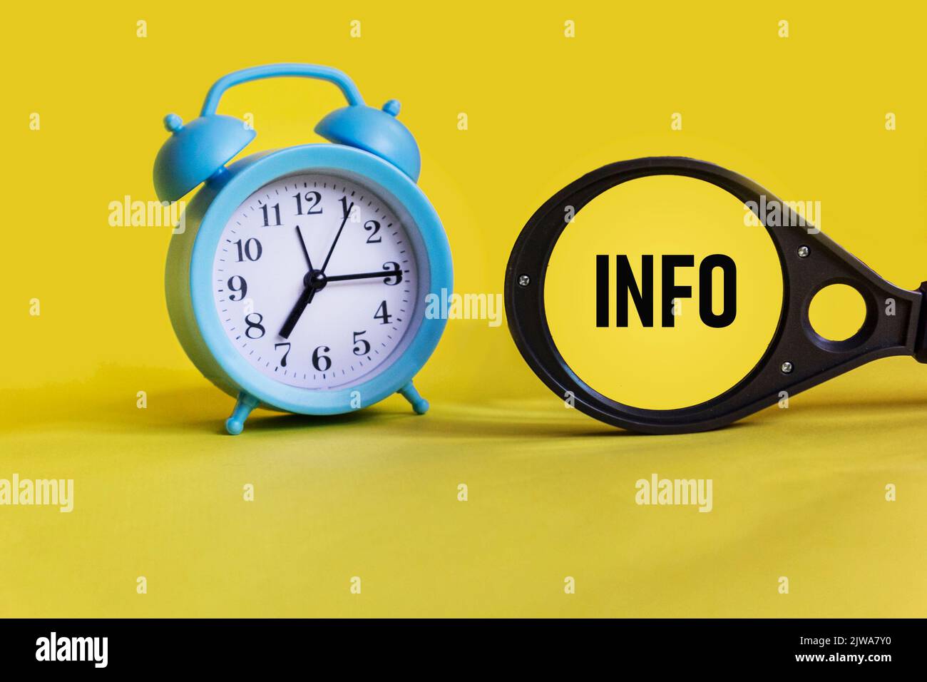 Info word on a magnifying glass on a yellow background with a clock. Business concept. Stock Photo