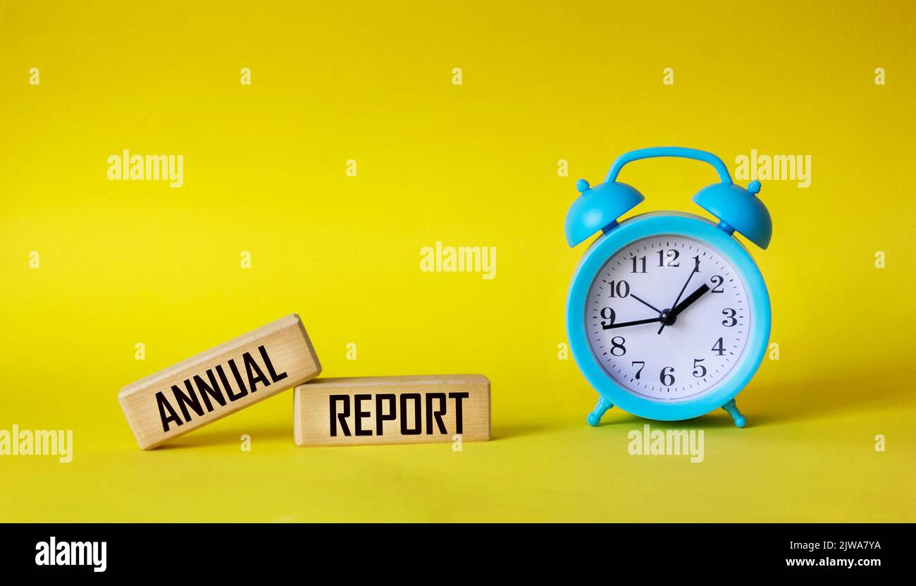The word annual report is written on a wooden block. Annual report text on yellow background with clock for your design, concept. Stock Photo