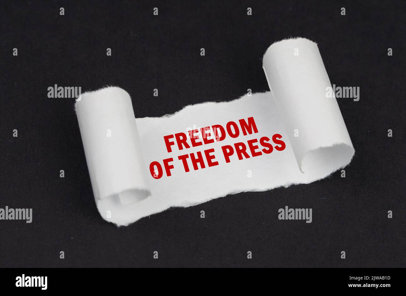 On a black surface lies a white twisted paper with the inscription - Freedom of the press Stock Photo
