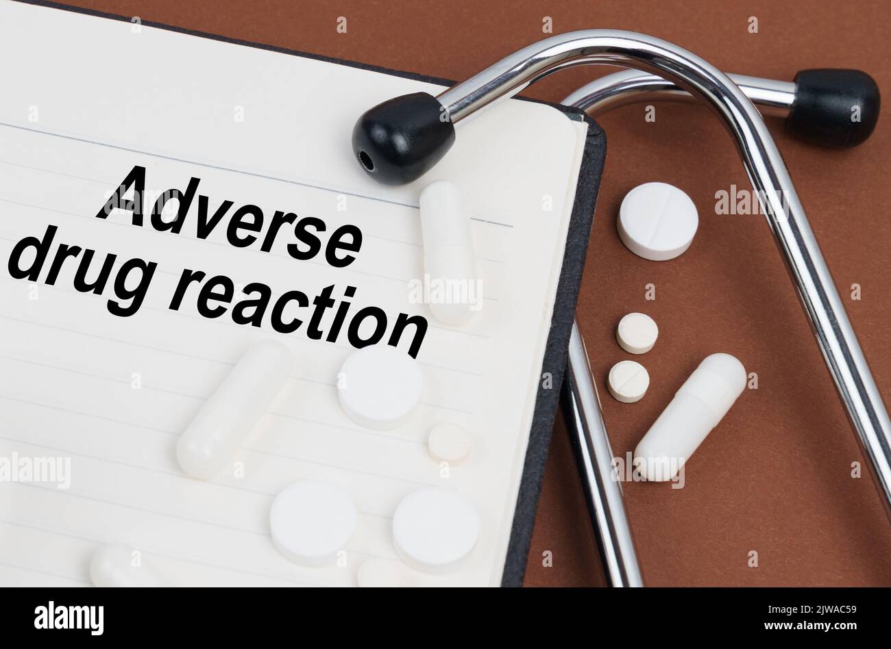 On a brown surface lies a stethoscope, pills and a notepad with the inscription - adverse drug reaction Stock Photo