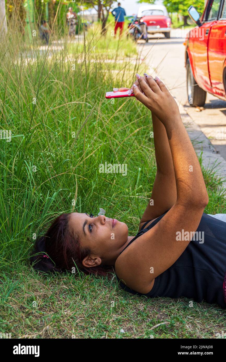 A 22 year old, Cuban, female, laying on grass and checking out her social media accounts. Havana, Cuba. Stock Photo
