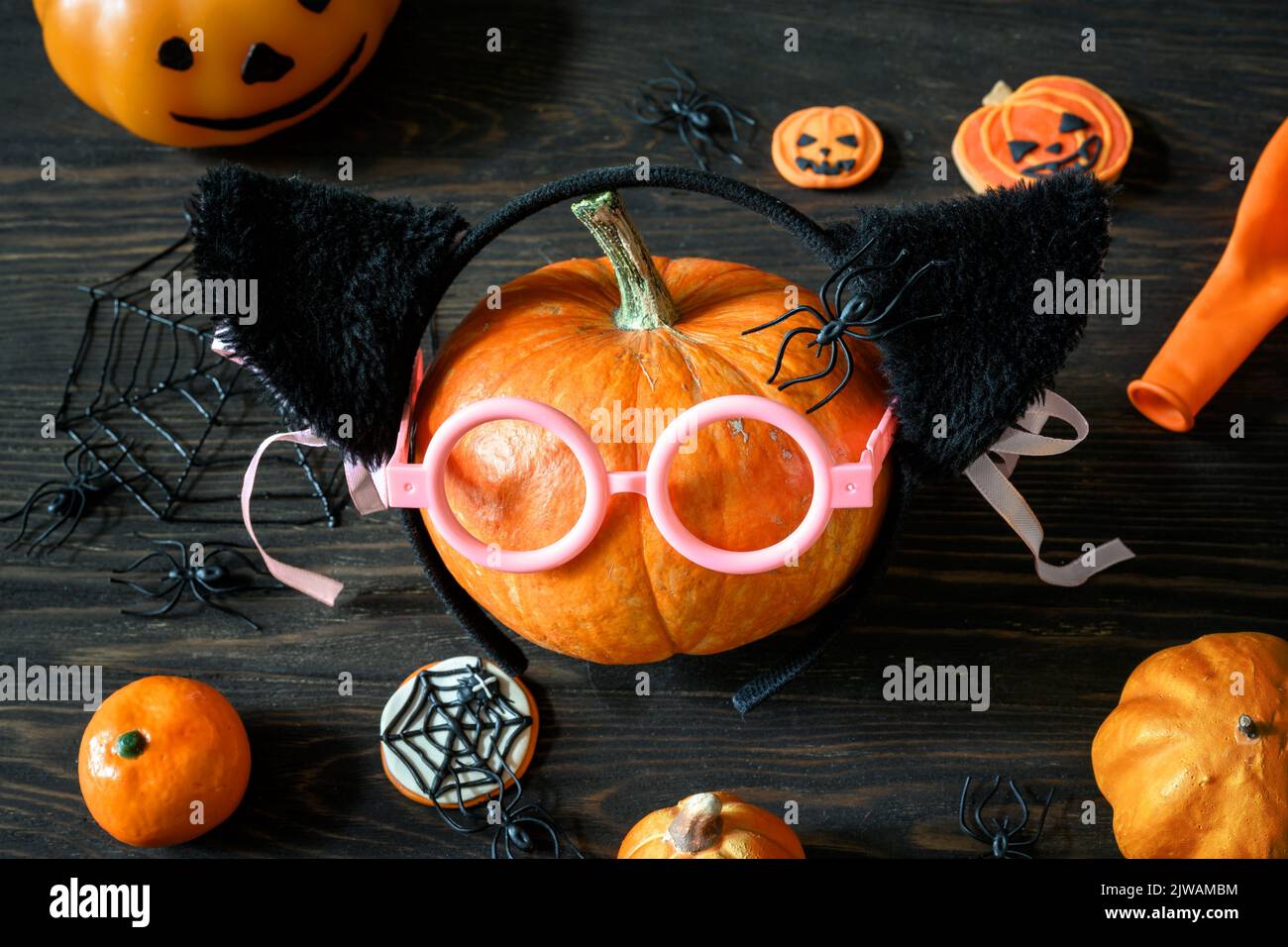 Halloween still life on wooden table, pumpkins and sweets on dark wood. Happy orange pumpkin with glasses, variety Halloween food and decorations. Lif Stock Photo