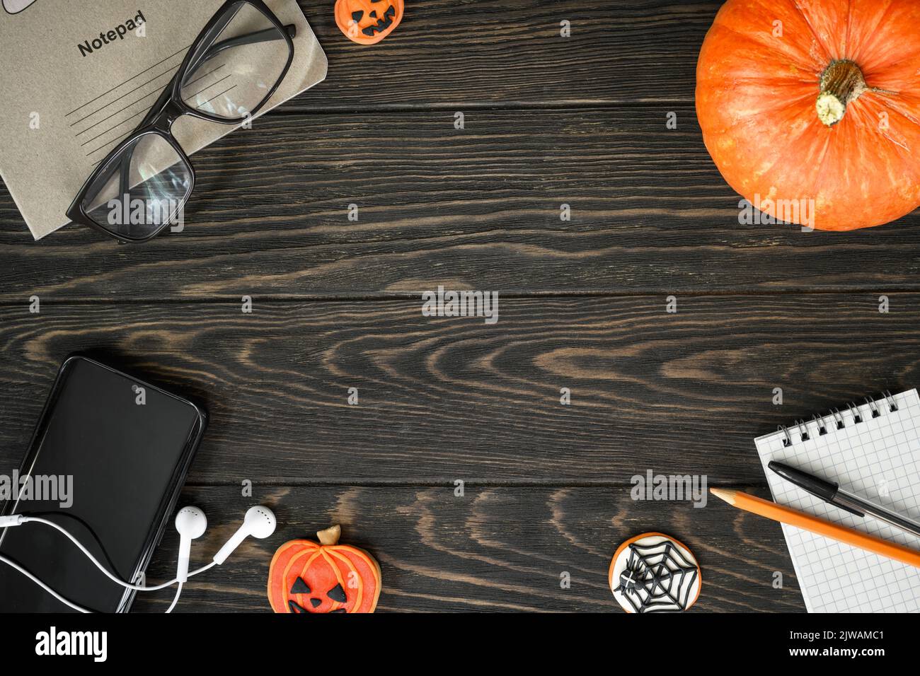 Halloween lifestyle background, top view. Pumpkin, sweets and accessories on dark wooden table, flat lay. Frame of Halloween food, glasses, phone on w Stock Photo