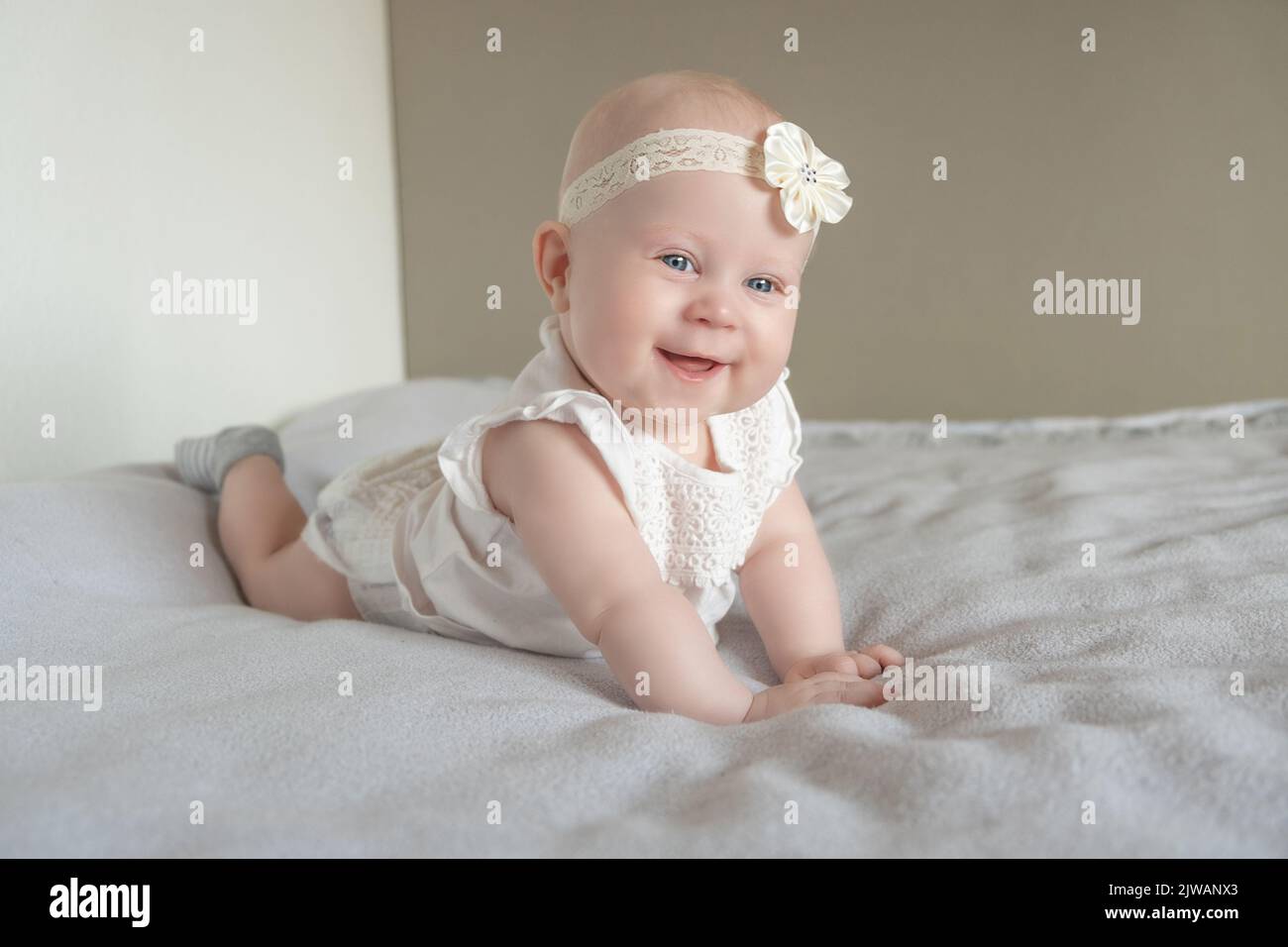 Portrait of a beautiful little baby girl lying on her stomach and looks away with admiration. Baby with big blue eyes. happy family concept Stock Photo