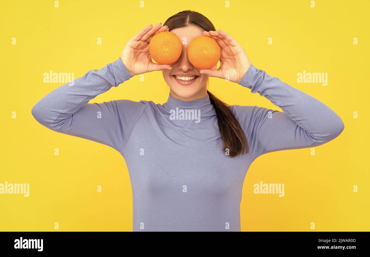 funny young woman holding orange citrus fruit on yellow background, vitamin Stock Photo