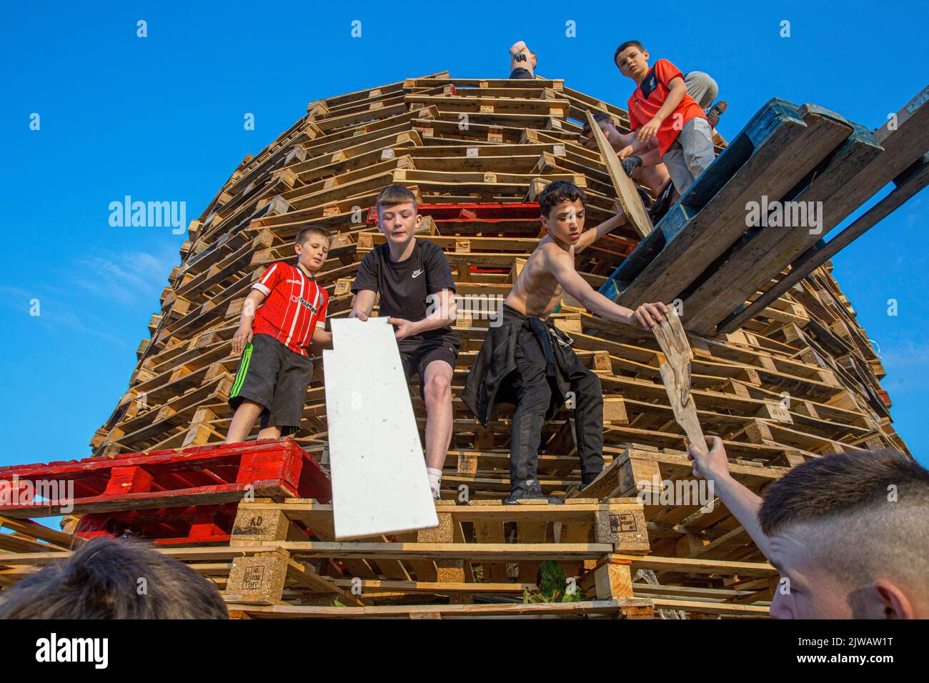 Kids stack pallets over the weekend in preparation for the bonfire marking a Catholic feast day of the Assumption of the Virgin Mary in the Bogside ar Stock Photo