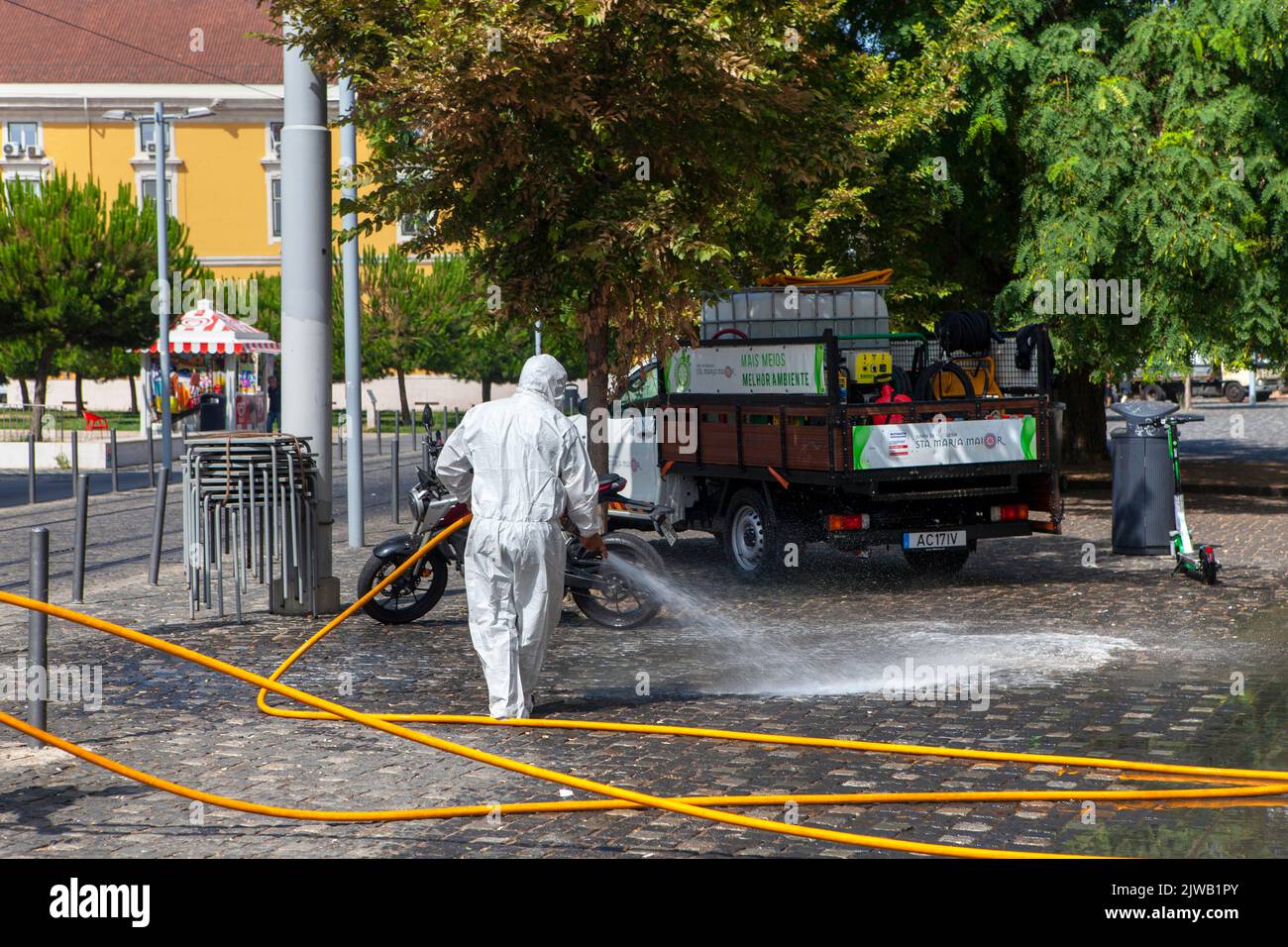 Full PPE white protective disposable suit Street cleaning with hose pipe in Lisbon Portugal Stock Photo