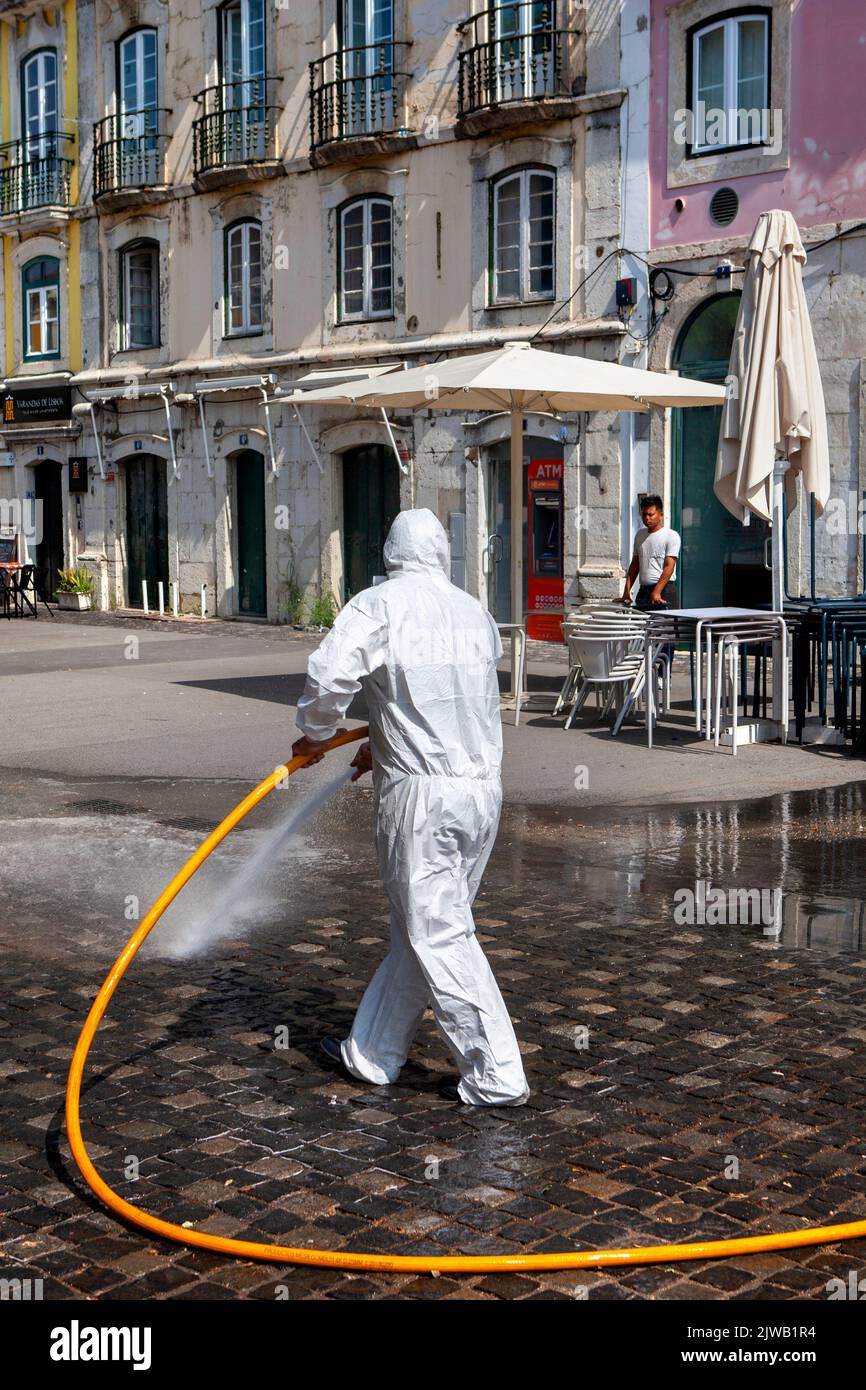 Full PPE white protective disposable suit Street cleaning with hose pipe in Lisbon Portugal Stock Photo
