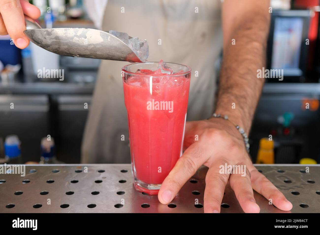 Hand of bartender serving fresh red, purple summer fruit cocktail with ice at bar counter on sunny day. Selected focus, shallow depth of field. Stock Photo