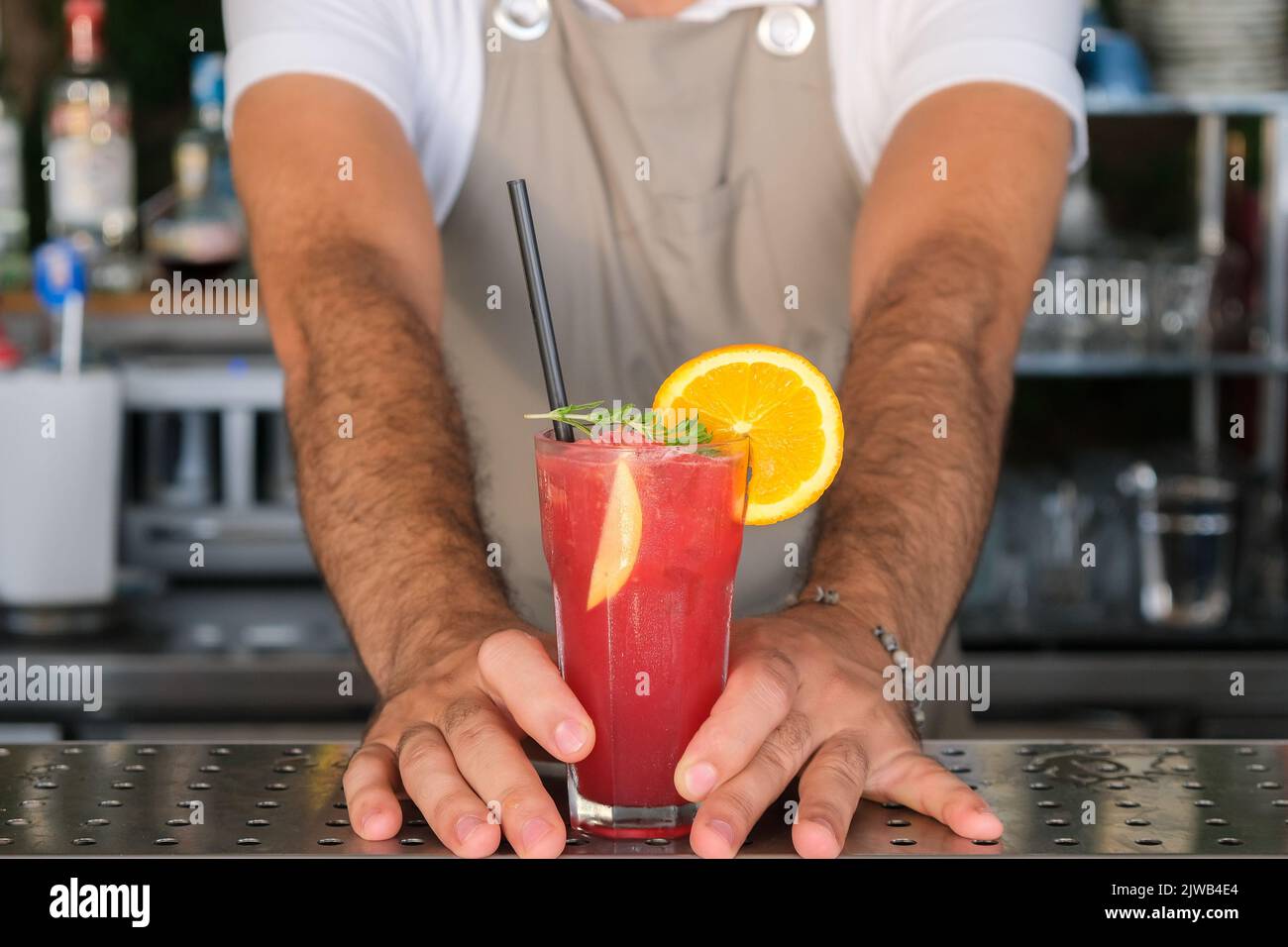 Hand of bartender serving fresh red, purple summer fruit cocktail at bar counter on sunny day, shallow depth of field, copy space. Stock Photo
