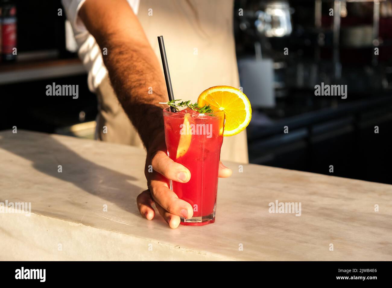 Hand of bartender serving fresh red, purple summer fruit cocktail at bar counter on sunny day, shallow depth of field, copy space. Stock Photo