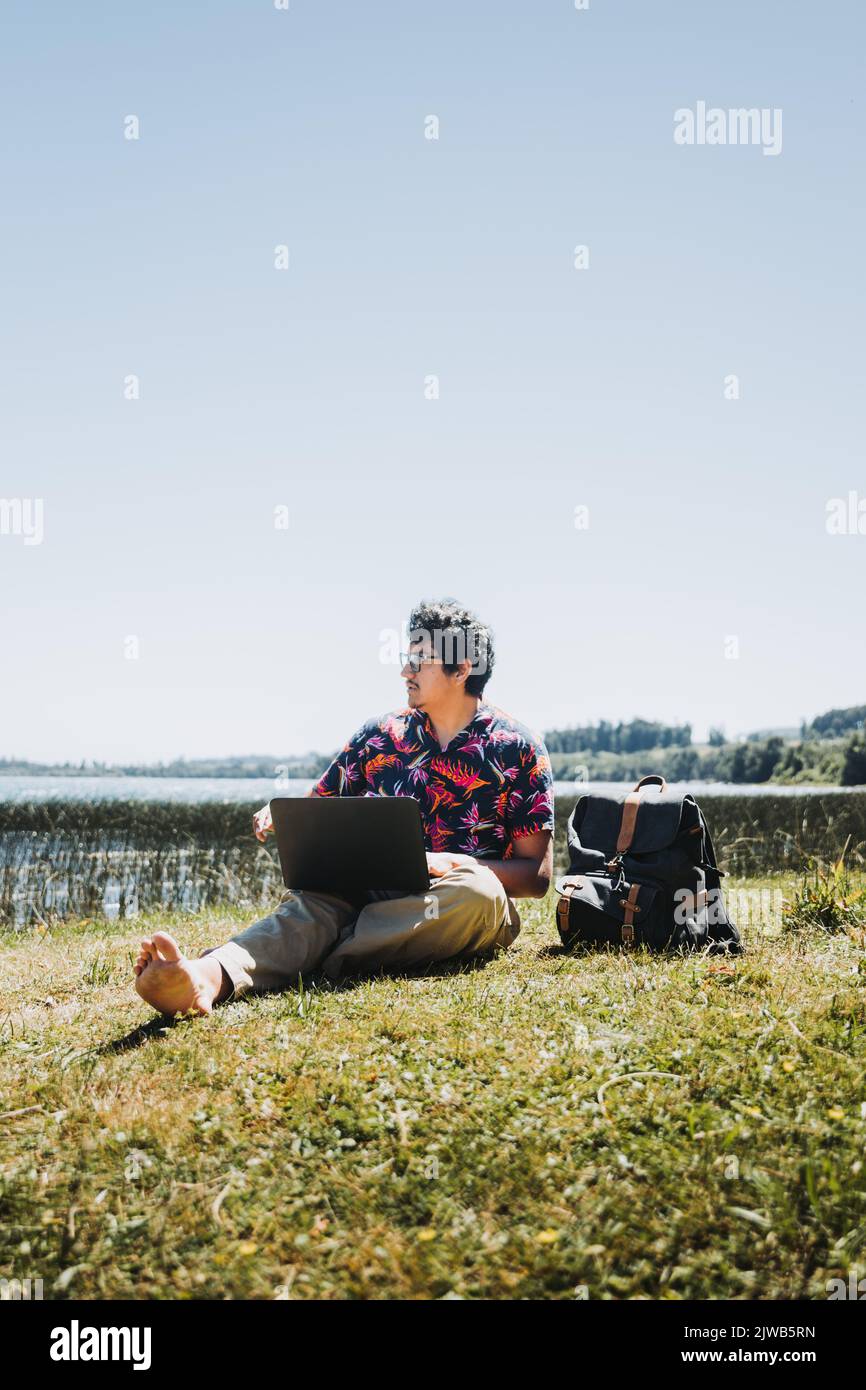 Front view young latin man doing remote online work from the lake. Teleworking concept. Digital nomad Stock Photo