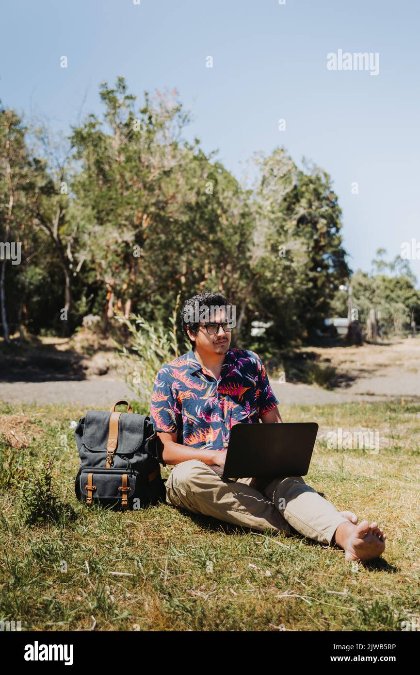 Front view young latin man doing remote online work from the lake. Teleworking concept. Digital nomad Stock Photo
