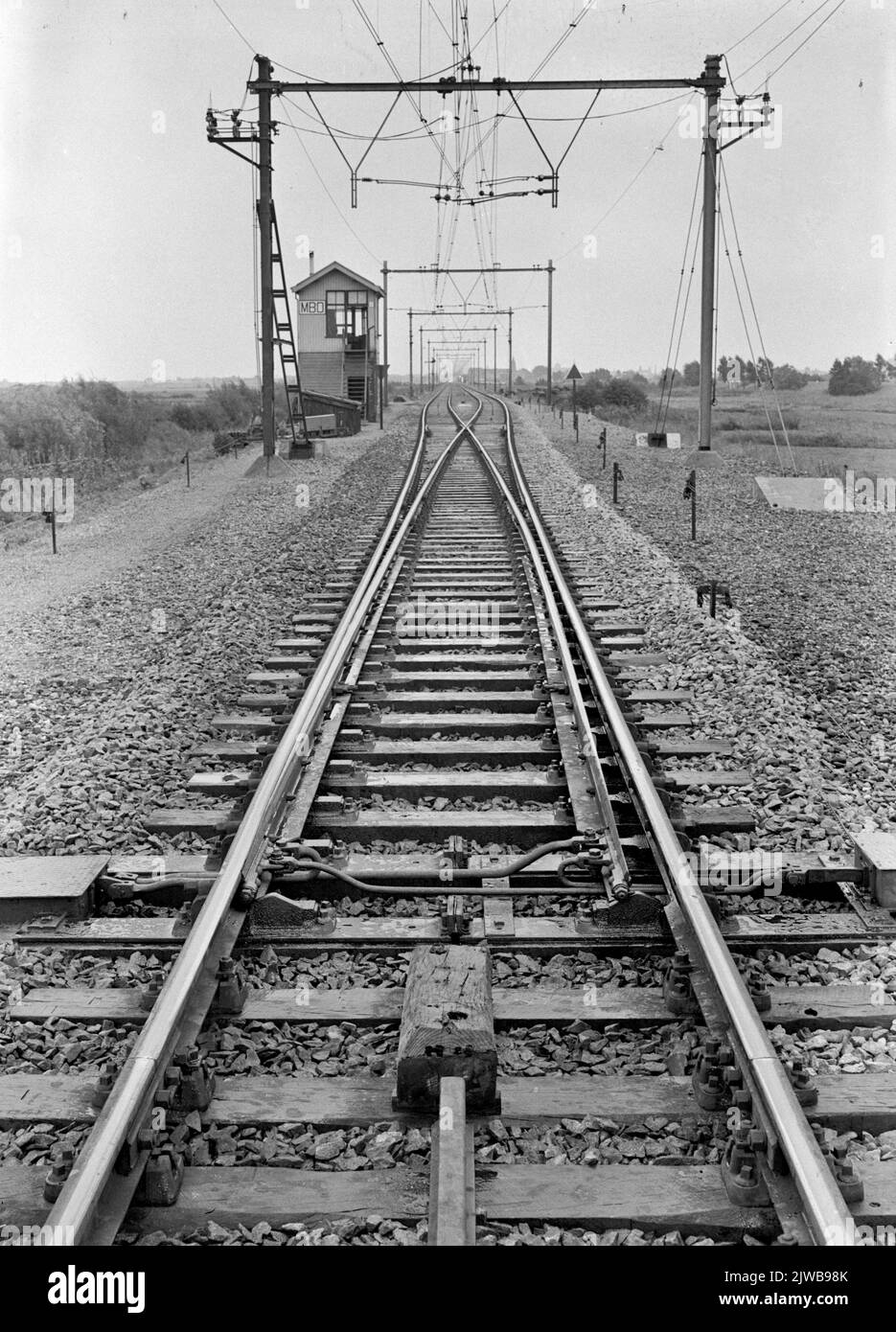 Image of the symmetrical switch for the transition to single -track at the railway bridge over the Maas in Hedel, with the Seinhuis MBO (Maas Bridge Transition) in the background. Stock Photo