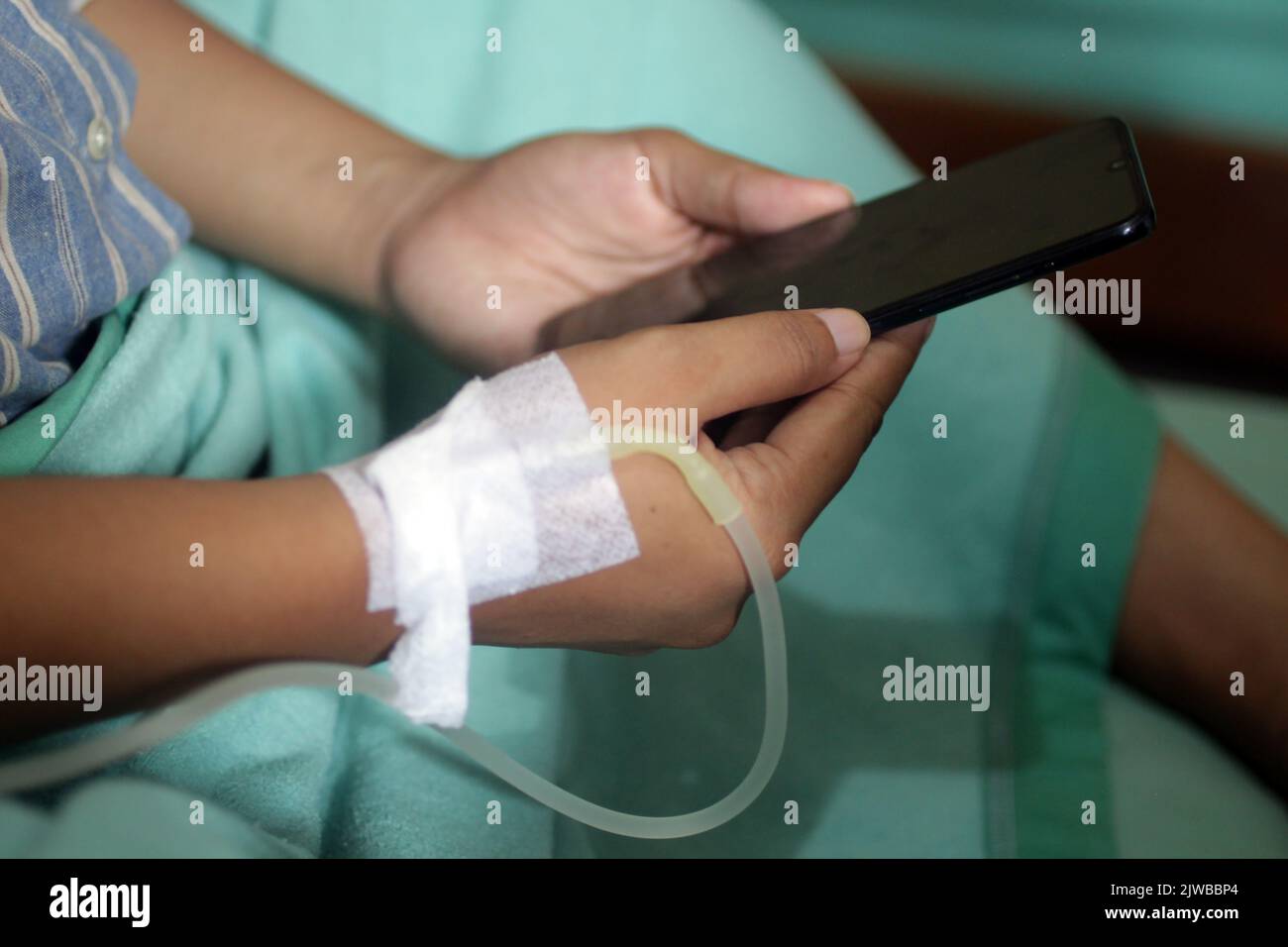 Female patient after giving baby birth, checking touchscreen phone with iv line on hand in the hospital. Stock Photo