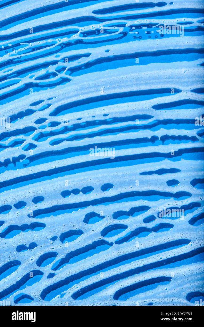 Top view of a blue glass surface covered with soap foam. Monochromatic background without people, concept of cleanliness. Stock Photo