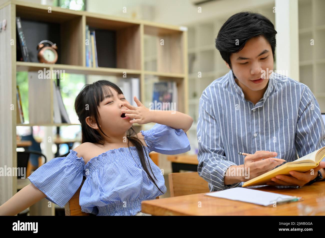 Pretty and charming young Asian girl yawning while her private tutor teaching math in the cafe. kindergarten or primary school kids. Stock Photo