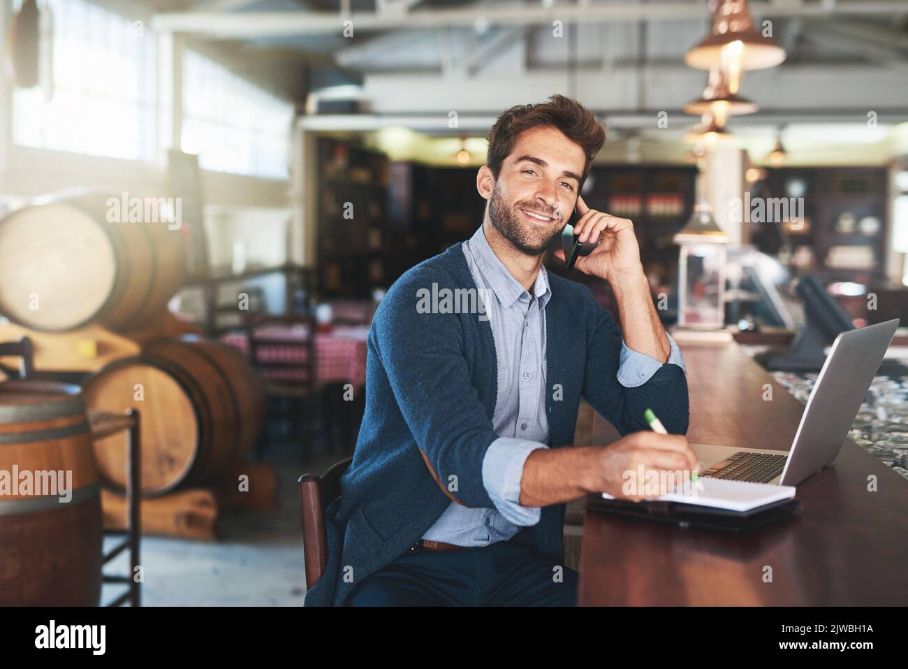 When would you like to meet. Cropped portrait of a handsome young man using his laptop and cellphone in a bar. Stock Photo