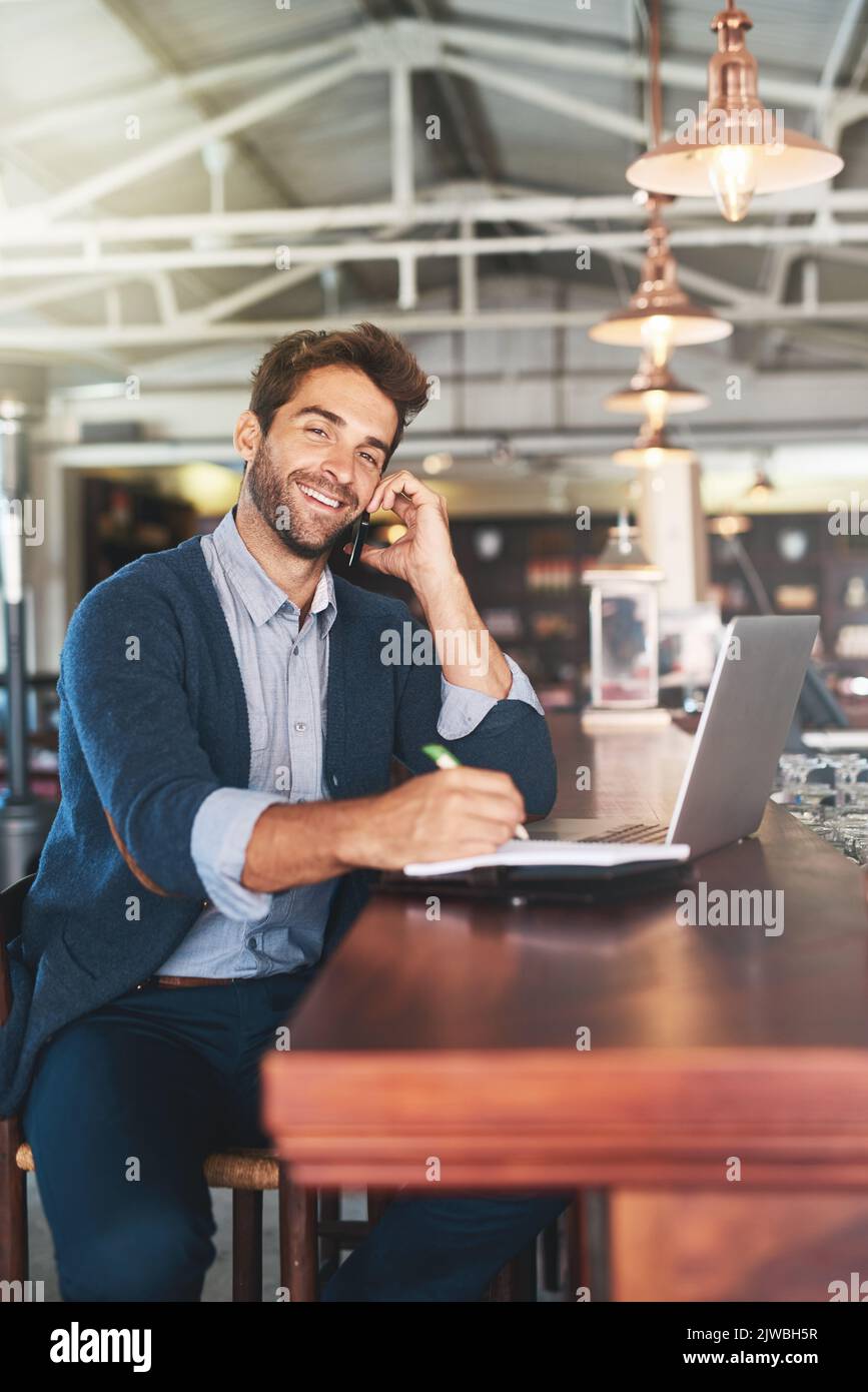 Meet me for a drink. Cropped portrait of a handsome young man using his laptop and cellphone in a bar. Stock Photo