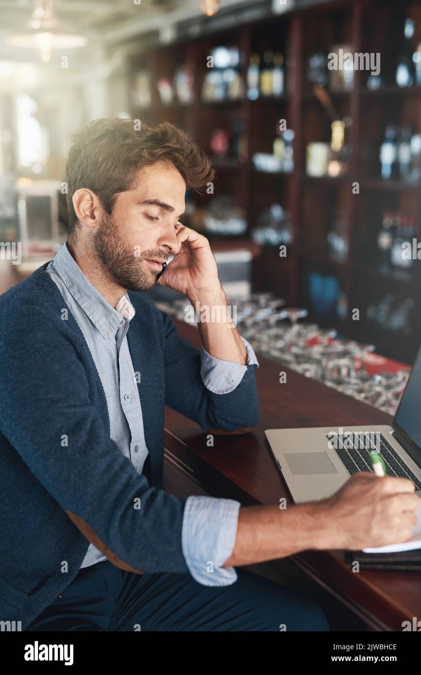 Give me the address...a handsome young man using his laptop and cellphone in a bar. Stock Photo