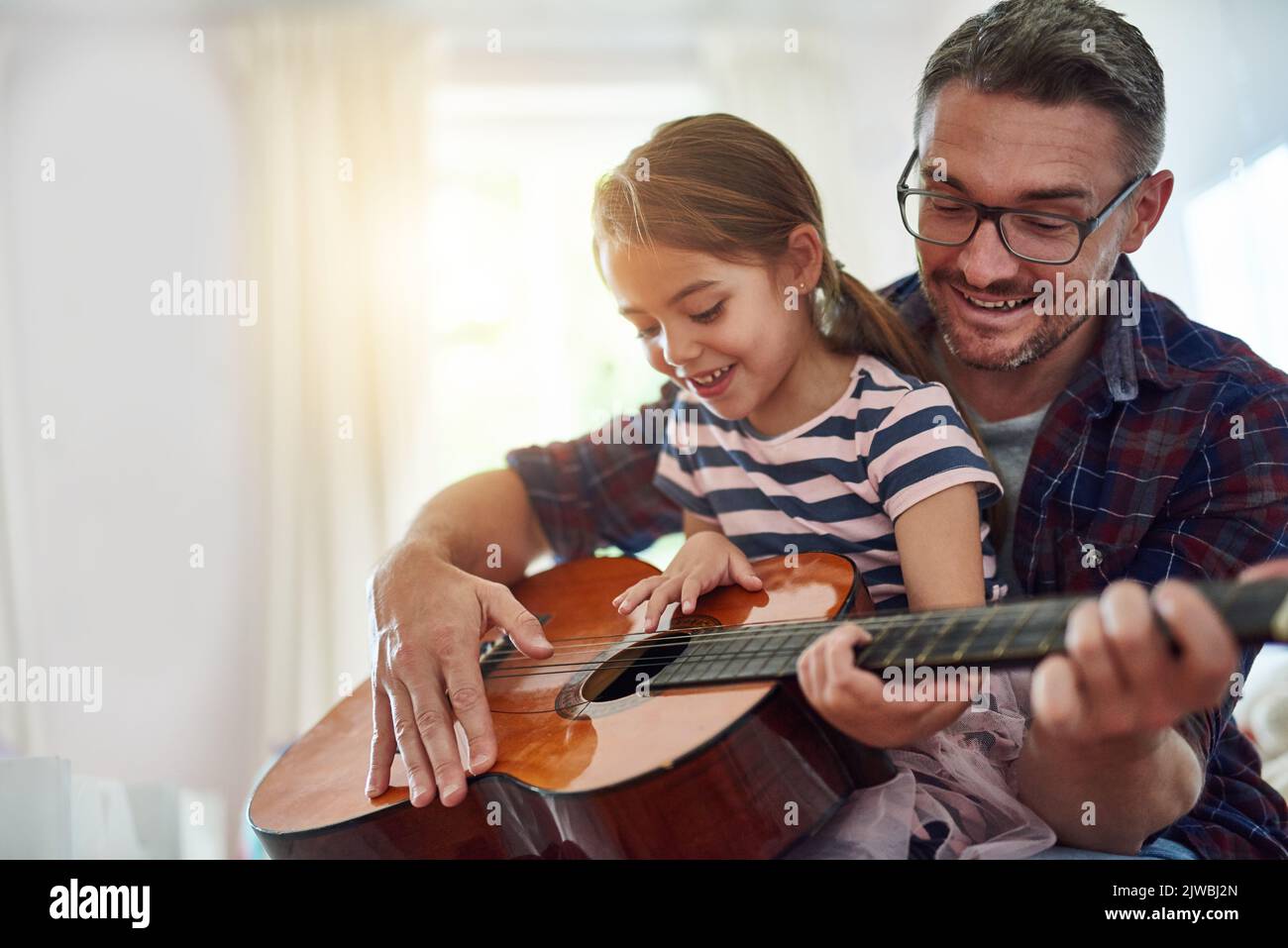 Shes worth the time spent. a little girl playing the guitar with her father. Stock Photo