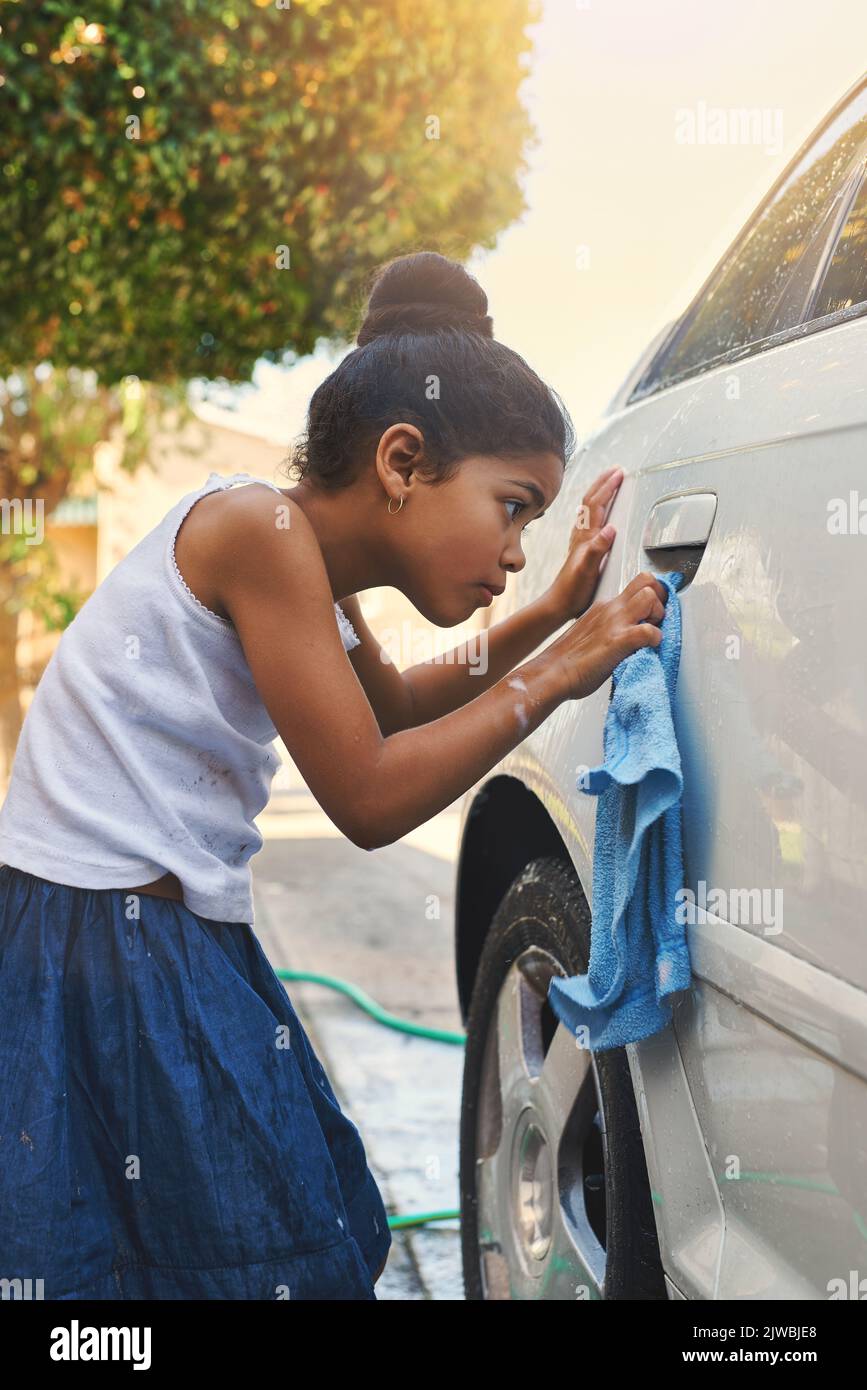 Making sure she doesnt miss a spot. a young girl busy cleaning a car outside. Stock Photo