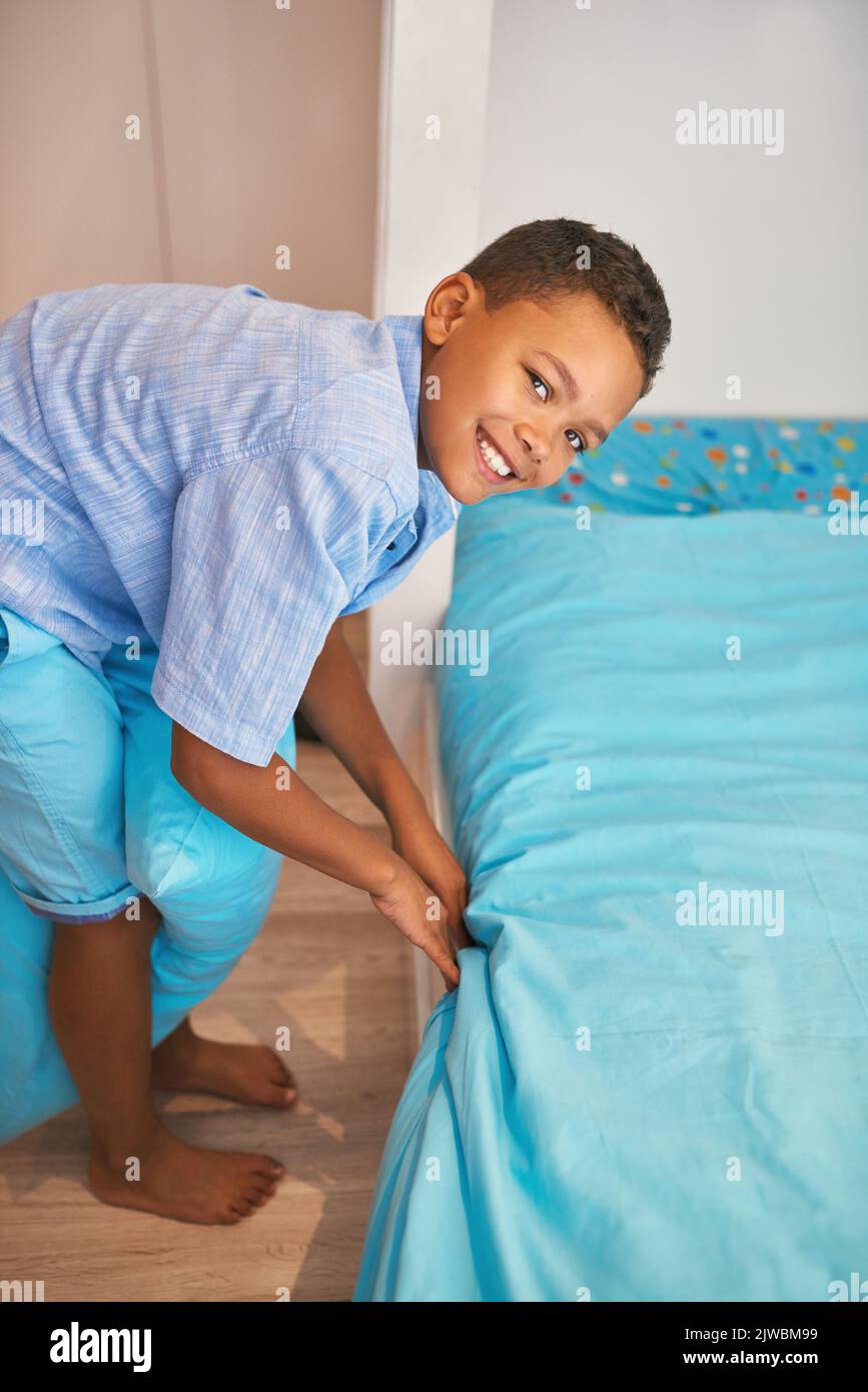 He keeps his room neat and tidy. Portrait of a young boy making up a bed. Stock Photo