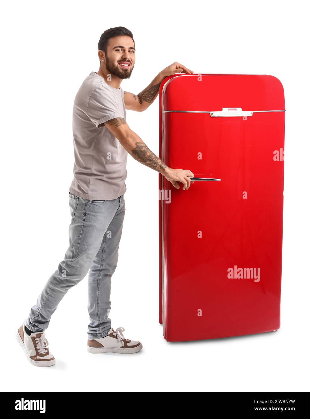 Cool tattooed young man opening red fridge on white background Stock Photo