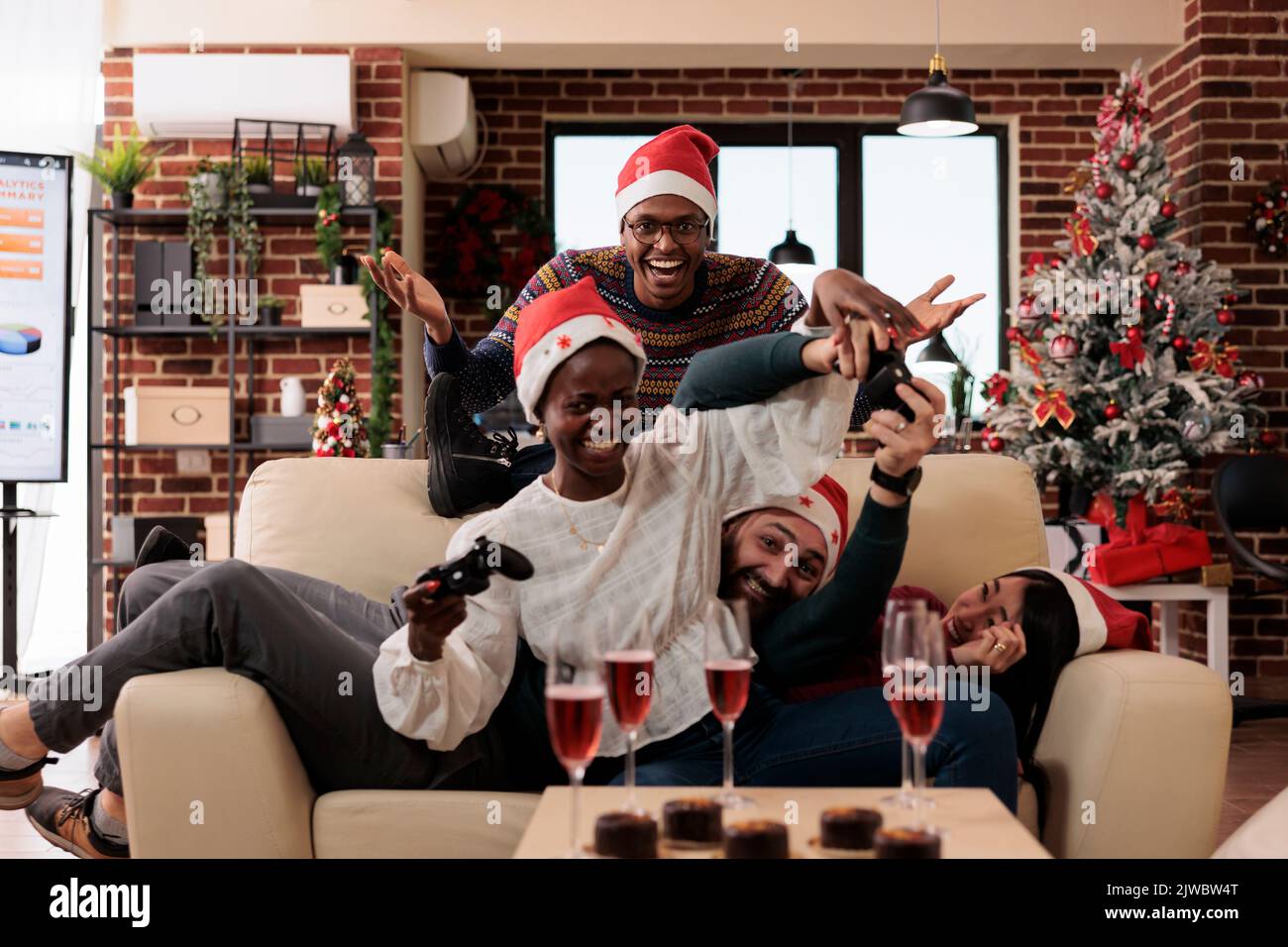 Diverse coworkers enjoying video games play on xmas day at office party event, celebrating christmas eve with gaming competition and alcohol. Colleagues having fun with console on winter holiday. Stock Photo