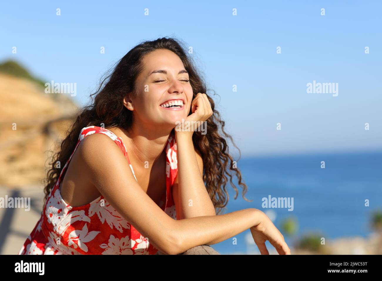 Happy woman in red dress laughing on the beach Stock Photo