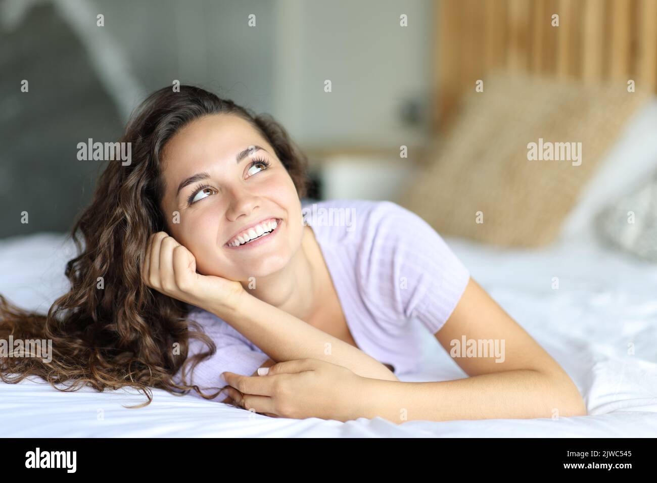 Happy woman looking at side and above lying on the bed Stock Photo