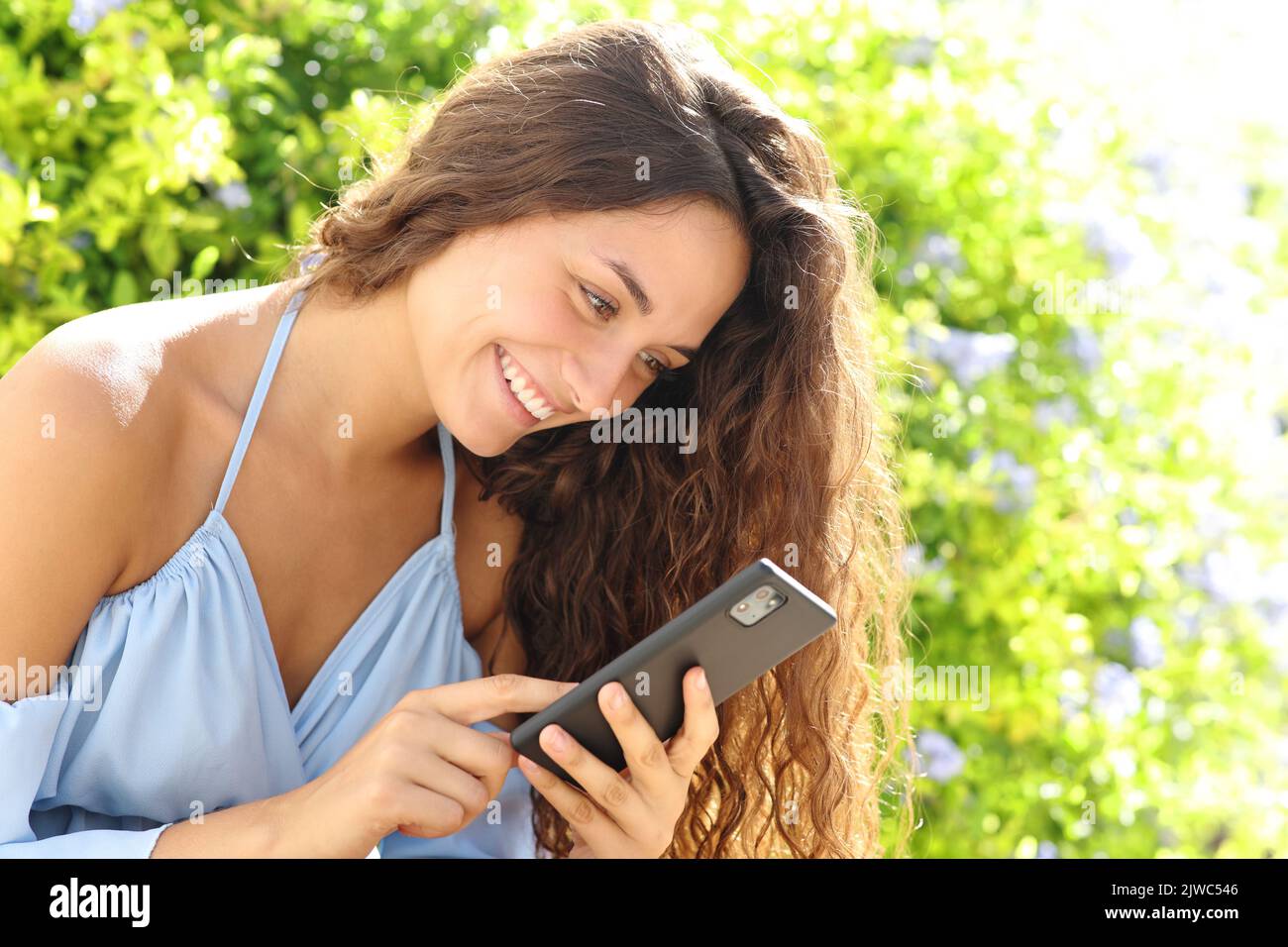 Happy woman in a green garden using smart phone Stock Photo
