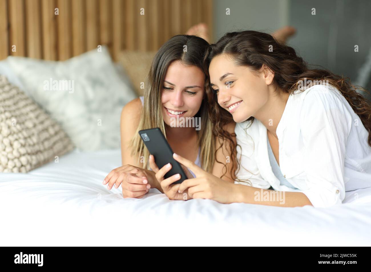 Two happy friends checking smartphone lying on a bed Stock Photo