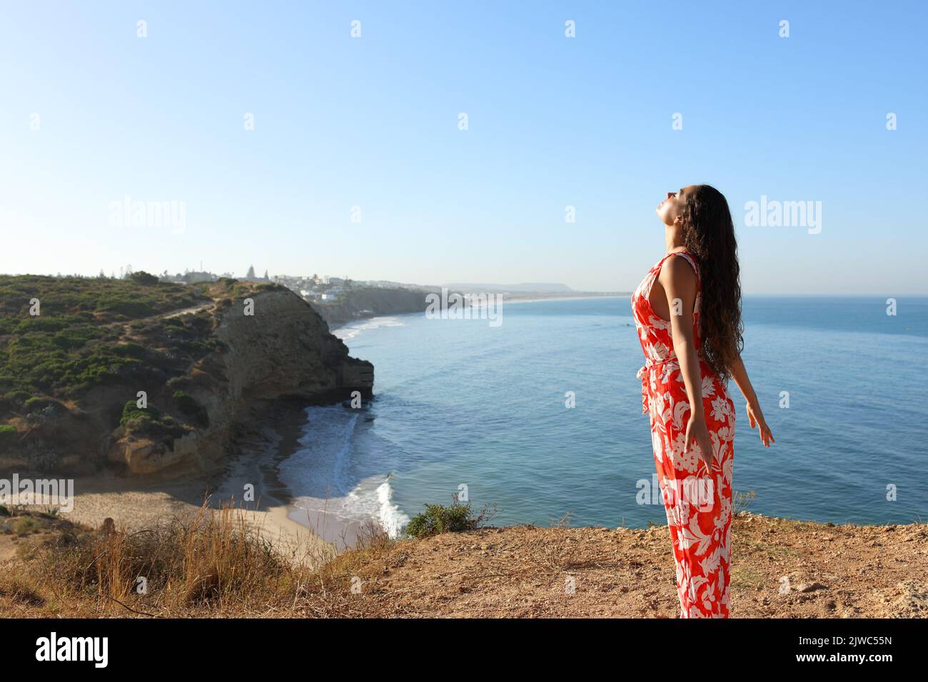 Woman in red dress breathing fresh air on a clif on the beach Stock Photo