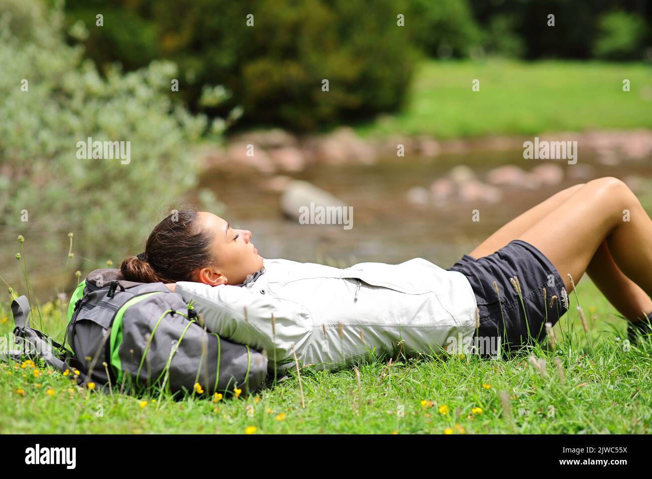 Side view portrait of a trekker resting lying on the grass in a riverside in the mountain Stock Photo