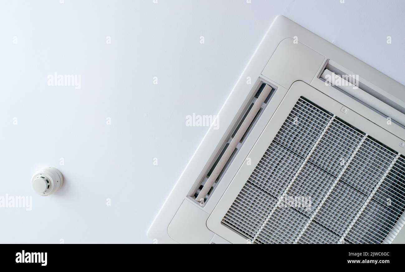 Cassette type air conditioner and smoke detector mounted on ceiling wall. Air duct on ceiling in hotel. Air heading unit on gypsum wall. Cool system i Stock Photo