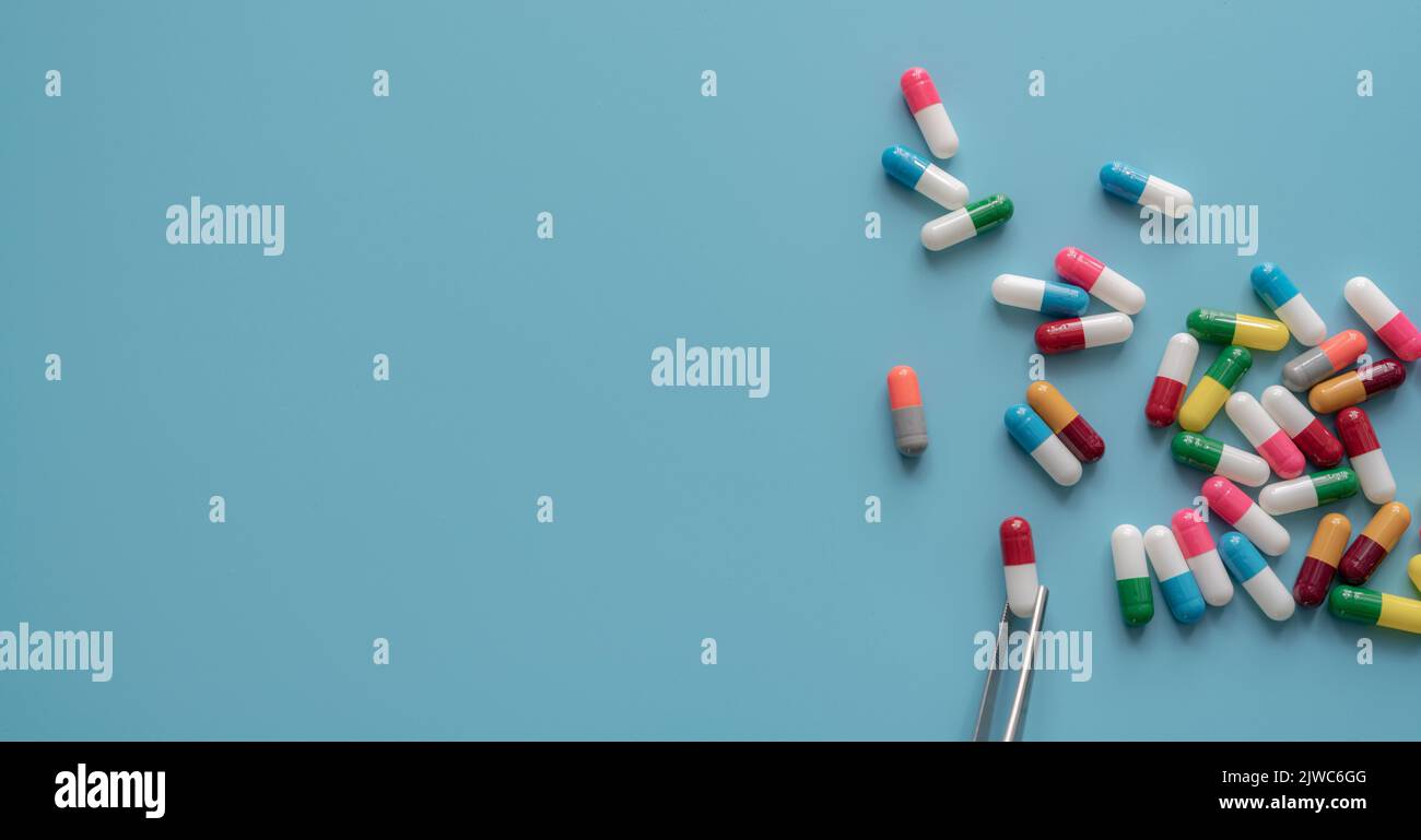Antibiotic drug selection. Multi-colored capsule pills on blue background. Forceps picks a red-white capsule up from many antibiotic capsule pills. Stock Photo