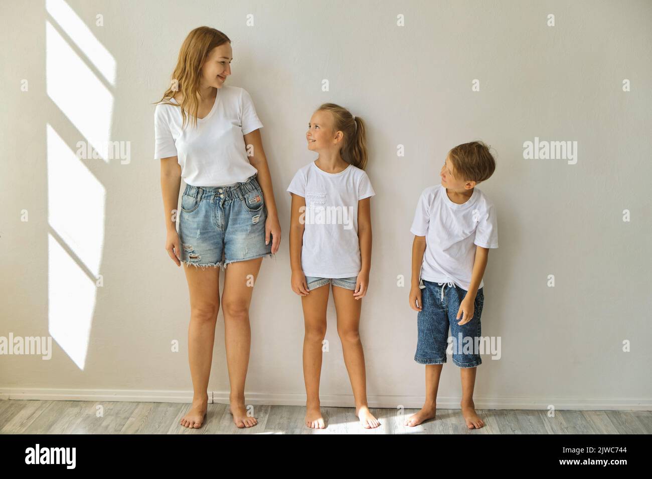 mother measures growth of kids to a daughter and son near light grey wall Stock Photo