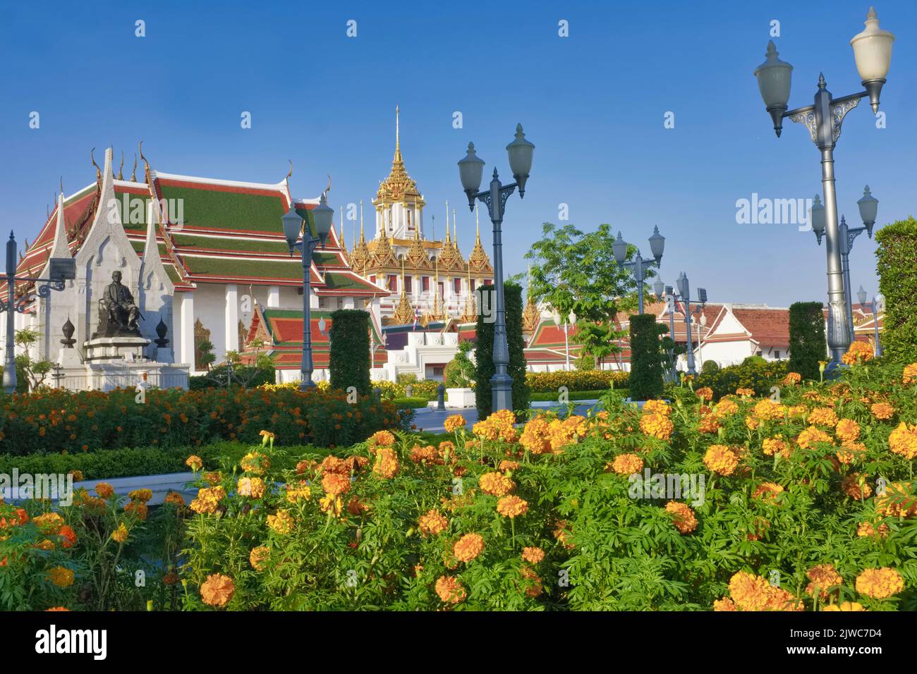The iconic Lohaprasad building (m), part of (temple) Wat Ratchanadta, with marigold flowers from an adjacent park in the foreground; Bangkok, Thailand Stock Photo