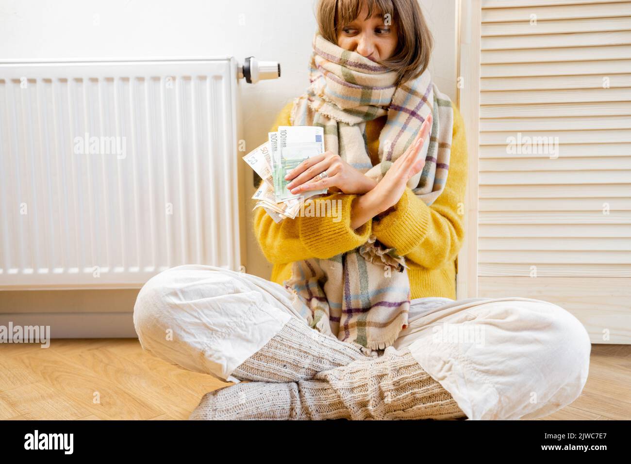 Upset warmly dressed woman with money near heater at home Stock Photo