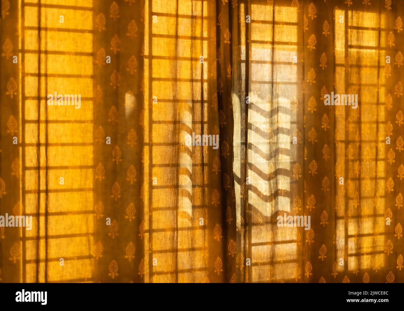 Morning sun casts a shadow of the window grille / grill on a curtain. Stock Photo