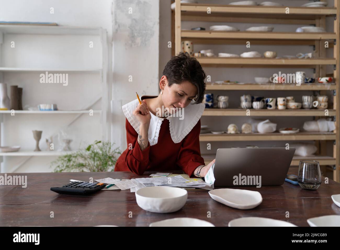 Focused young woman ceramic studio owner analyzing bills and receipts