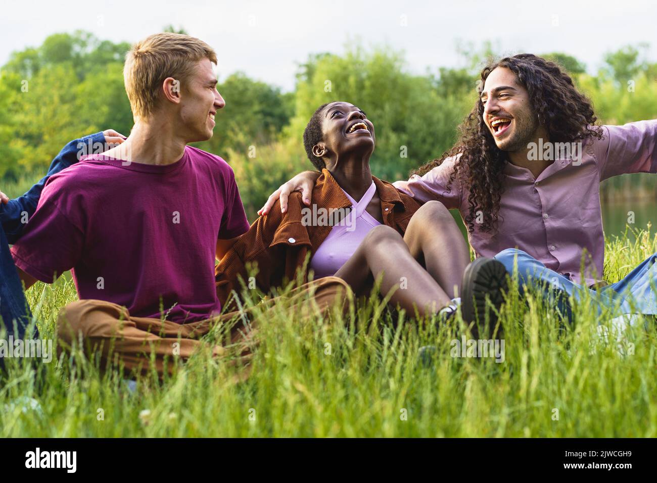 Cheerful multiethnic friends bonding and having fun hugging and laughing on the grass having fun together - Group of cheerful multiracial gen z young Stock Photo